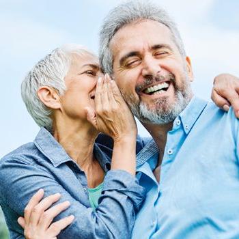 A retiree playfully whispers into her partner's ear as he laughs.